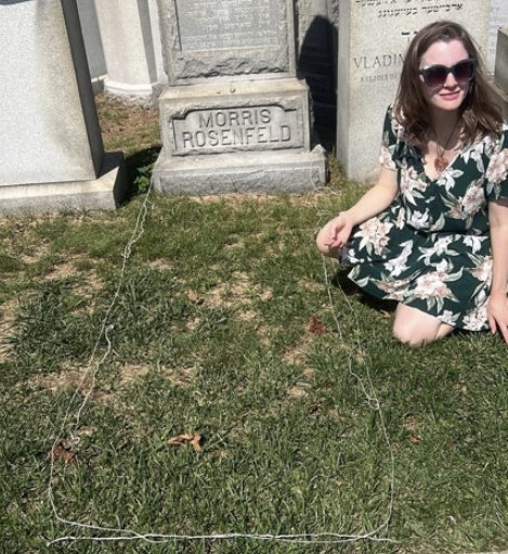 a woman sits on the grass next to a grave which is outlined by thread